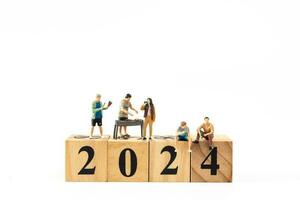 Miniatur Menschen , ein froh Familie genießt Neu Jahre Feierlichkeiten mit hölzern Block 2024 foto