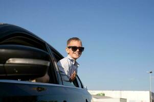 ein süß Junge im Sonnenbrille sah aus von das Auto Fenster mit ein Lachen foto