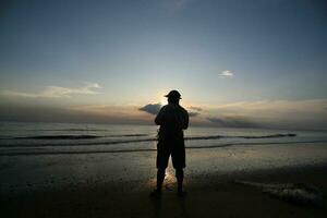 das Schönheit von das Sonnenuntergang auf das Strand mit das Silhouette von ein Fischer foto