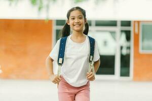 Porträt von ein lächelnd wenig asiatisch Mädchen mit Rucksack beim Schule foto