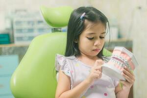 asiatisch Mädchen im Dental Stuhl, mit Zahn Bürste. Medizin, Zahnheilkunde und Gesundheitswesen Konzept foto