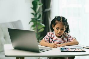 asiatisch wenig Mädchen mit Laptop und tun Hausaufgaben im Leben Zimmer beim Zuhause foto