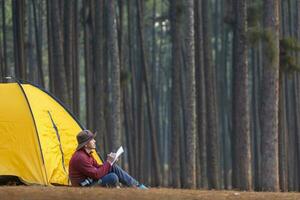 Solo über Nacht Camping während Sitzung neben Zelt beim Campingplatz im das Kiefer Wald während Schreiben Tagebuch zum Freiheit, Einsamkeit, friedlich Entspannung Flucht zu Wildnis und Natur Heilung Therapie foto