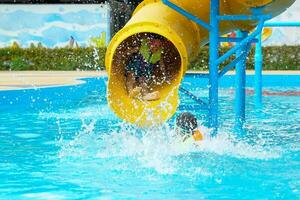 Kinder abspielen Wasser Folien im das Wasser Park. er war glücklich und haben Spaß, insbesondere wann er rutschte aus in das Schwimmbad und das Wasser bespritzt. Sanft und selektiv Fokus. foto