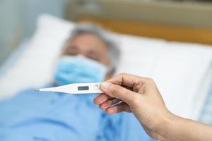 Arzt, der ein digitales Thermometer hält, um asiatische Senioren oder ältere ältere Frauen zu messen, die eine Gesichtsmaske tragen, haben Fieber im Krankenhaus, gesundes, starkes medizinisches Konzept.