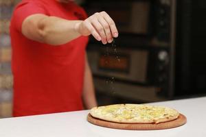Der Koch bereitet die Pizza zu und bestreut sie mit Gewürzen. das Konzept von leckerem Essen und gesundem Essen. auf schwarzem Hintergrund für Design oder Beschriftungstext. selektiver Fokus foto
