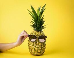 saftig Ananas mit Sonnenbrille, Sommer- Ferien Konzept, weiblich Hand, Gelb Hintergrund - - nahrhaft Frucht. foto