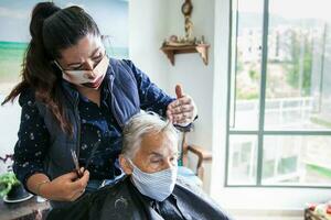 Senior Frau bekommen ein Haarschnitt beim Zuhause während covid19 Pandemie tragen Gesicht Maske foto