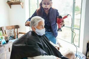 Senior Frau bekommen ein Haarschnitt beim Zuhause während covid19 Pandemie tragen Gesicht Maske foto