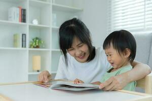 glücklich Asien Mutter lesen Geschichte Buch zum wenig Kind. Familie ist glücklich und aufgeregt im das Haus. Mutter und Tochter haben Spaß Ausgaben Zeit zusammen. Urlaub, Aktivität, Exekutive Funktion, Ich, Gl foto