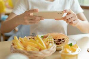 Restaurant Inhaber nimmt ein Bild von das Essen auf das Tabelle mit ein Smartphone zu Post auf ein Webseite. online Essen Lieferung, Bestellung Service, Beeinflusser, Rezension, Sozial Medien, Aktie, Marketing, Interesse. foto