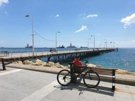 Ein Mann sitzt auf einer Bank hinter einem Fahrrad und blickt auf das Meer an der Promenade von Molos in Limassol, Zypern