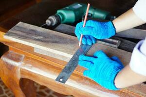 schließen oben Zimmermann Hände trägt Blau Handschuhe ist Messung Holz Tafel durch mit Bleistift und Herrscher. Konzept , Zimmermann Arbeiten, Konstruktion, Design, selbstgemacht. renovieren Holzarbeiten beim heim, Zimmerei. foto