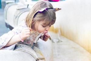 kleines Mädchen trinkt Wasser am öffentlichen Brunnen
