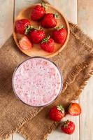 frischer Milchshake mit Erdbeeren. Sommergetränk mit Beeren in einem Glas auf Holzhintergrund.