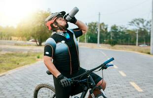 müde Radfahrer Trinken Wasser draußen. mollig Radfahrer auf seine Fahrrad Trinken Wasser, durstig Radfahrer auf seine Fahrrad Trinken Wasser außen. foto