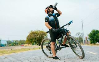 mollig Radfahrer auf seine Fahrrad Trinken Wasser, durstig Radfahrer auf seine Fahrrad Trinken Wasser außen. müde Radfahrer Trinken Wasser draußen foto