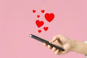 weiblich Hände halten Handy, Mobiltelefon Telefon mit Herzen, Liebe Symbol auf Rosa Hintergrund. Valentinstag Tag Konzept. foto