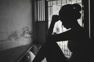 Silhouette von deprimiert jung Frau in der Nähe von Fenster beim heim, Nahansicht im das dunkel Zimmer. inländisch Gewalt, Gewalt gegen Frauenschwarz und Weiß Foto. foto