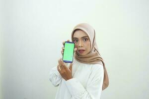 aufgeregt schön asiatisch Muslim Frau zeigen Grün Bildschirm Handy, Mobiltelefon Telefon isoliert Über Weiß Hintergrund foto