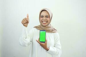 aufgeregt schön asiatisch Muslim Frau zeigen Grün Bildschirm Handy, Mobiltelefon Telefon isoliert Über Weiß Hintergrund foto