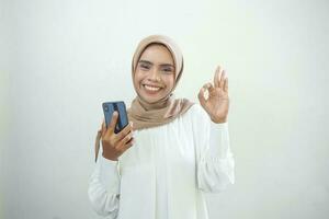 aufgeregt schön asiatisch Muslim Frau zeigen Handy, Mobiltelefon Telefon isoliert Über Weiß Hintergrund foto