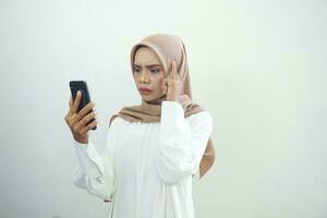 aufgeregt und Denken schön asiatisch Muslim Frau zeigen Handy, Mobiltelefon Telefon isoliert Über Weiß Hintergrund foto