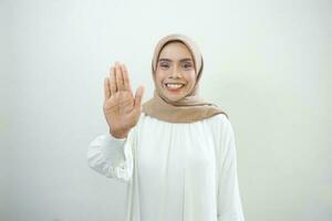 ernst jung asiatisch Muslim Frau gekleidet im beiläufig Weiß Stehen mit ausgestreckt Hand zeigen halt Geste isoliert Über Weiß Hintergrund foto