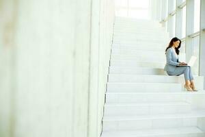 jung Geschäft Frau Sitzung auf das Treppe auf Büro Flur und Arbeiten auf Laptop foto