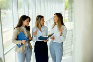drei jung Geschäft Frauen haben ein Diskussion während Gehen im das Büro Flur foto