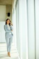 jung Frau mit Handy, Mobiltelefon Telefon durch das Büro Fenster foto