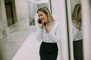 jung Geschäft Frau mit Handy, Mobiltelefon Telefon im das Büro Flur foto