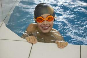 ein Junge im ein Schwimmen Deckel und Brille im das Schwimmbad. er lächelt und sieht aus in das Kamera. Kind im das Sport Schwimmbad. foto