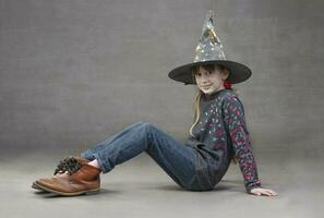 wenig Mädchen im Jeans Hexe Hut und komisch Stiefel. Kind beim das Halloween Party. foto