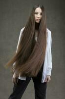 schön Brünette Mädchen mit sehr lange und glatt Haar auf ein grau Hintergrund. luxuriös Haar Länge. foto