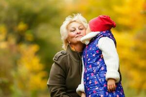 glücklich Senior Dame und ein wenig Kleinkind Mädchen, Oma und Enkelin, genießen ein gehen im das Park. Kind und Großelternteil. Herbst Tag. Oma und wenig Mädchen glücklich zusammen im das Garten foto