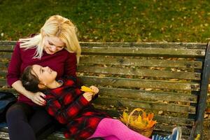 glücklich Mutter und Tochter Umarmen auf ein Bank im ein Herbst Park foto