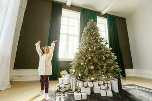 ziemlich wenig Mädchen lächelnd mit Geschenk in der Nähe von das Weihnachten Baum foto