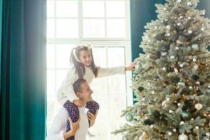 glücklich Vater und seine wenig Tochter dekorieren das Weihnachten Baum beim heim. foto