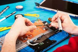 Zauberer repariert Laptop mit Werkzeugen und Händen auf dem blauen Holztisch. Ansicht von oben foto