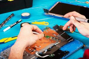 Zauberer repariert Laptop mit Werkzeugen und Händen auf dem blauen Holztisch. Ansicht von oben foto