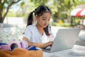 wenig Mädchen Verwendet ein Laptop zu lernen beim Schule. das Kind lächelt glücklich und bekommt Wissen entfernt. foto