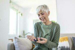 Reife Frau, die auf hohen Blutzucker testet. Frauenhaltevorrichtung zur Messung des Blutzuckers. Frau macht Blutzuckertest. Frau, die zu Hause den Blutzuckerspiegel mit Glukometer und Teststreifen überprüft foto