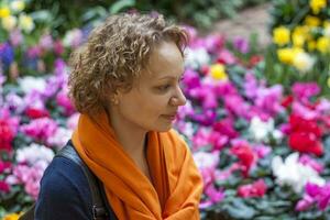 Porträt von ein lockiges Haar Mädchen auf das Hintergrund von ein Blume Bett. Nahansicht von das Gesicht von ein jung schön Frau. ein Mädchen mit lockig Haar und ein Orange Schal um ihr Nacken. foto