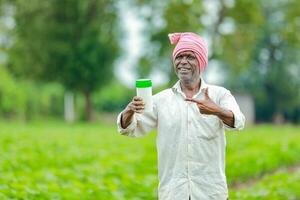 indisch glücklich Farmer halten leeren Flasche im Hände, glücklich Farmer zeigen Weiß Flasche foto