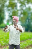 indisch glücklich Farmer halten leeren Flasche im Hände, glücklich Farmer zeigen Weiß Flasche foto