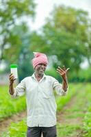 indisch glücklich Farmer halten leeren Flasche im Hände, glücklich Farmer zeigen Weiß Flasche foto