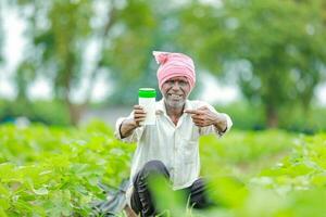 indisch glücklich Farmer halten leeren Flasche im Hände, glücklich Farmer zeigen Weiß Flasche foto