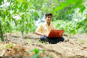 indisch Junge studieren im Bauernhof, halten Laptop im Hand , Arm indisch Kinder foto