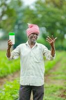 indisch glücklich Farmer halten leeren Flasche im Hände, glücklich Farmer zeigen Weiß Flasche foto